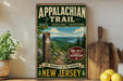 A vintage-style metal sign for the Appalachian Trail, featuring a scenic mountain landscape and a trail marker, is displayed on a shelf next to a wooden cutting board and some lemons.