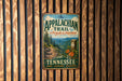 A vintage metal sign for the Appalachian Trail in Tennessee, featuring a scenic mountain landscape and the trail's name.