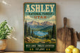 A vintage-style poster of the Ashley National Forest in Utah, featuring a scenic mountain landscape with pine trees and a lake.