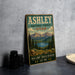 A vintage-style sign for the Ashley National Forest in Utah, featuring a scenic landscape with mountains, pine trees, and a lake.