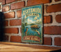 A vintage-style metal sign with a tropical landscape and a boat, mounted on a brick wall.