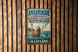 A vintage metal sign for Assateague Island National Seashore, Maryland, featuring a lighthouse and a horse in the water.