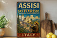 a vintage-style sign for the Basilica of San Francisco, Italy, with a painting of a man in a brown robe and hat, holding a book, and standing in front of a church.