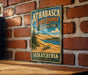 A vintage metal sign for Athabasca Sand Dunes Provincial Park in Saskatchewan, Canada, featuring a scenic landscape with sand dunes, a lake, and pine trees.