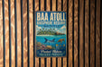 A vintage metal sign with the text "BAA ATOLL BIOSPHERE RESERVE MALIVES" and an illustration of a tropical island with various marine life, such as a shark, turtle, and fish, against a backdrop of a blue ocean.