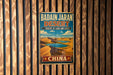 A vintage metal sign for the Badain Jaran Desert in China, featuring a desert landscape with sand dunes and a lake.