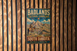 A vintage metal sign for Badlands Cultural Landscape South Dakota, featuring a cowboy on horseback and a mountain landscape.