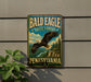 A metal sign with the text "Bald Eagle State Forest Pennsylvania" and an illustration of a bald eagle in flight, mounted on a wall.