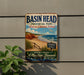 A vintage-style metal sign for Basin Head Provincial Park, Prince Edward Island, featuring a beach scene with a bird flying overhead and a sign indicating "Singing Sands".