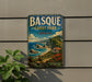 A vintage-style metal sign for Basque Coast Park in Spain, featuring a scenic coastal landscape with cliffs, a beach, and a small house.