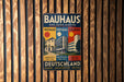 A vintage metal sign for the Bauhaus in Deutschland, featuring a colorful illustration of the Bauhaus buildings and text in German.