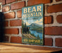 A vintage-style metal sign with the text "BEAR MOUNTAIN STATE FOREST" and "NEW HAMPSHIRE" is displayed on a brick wall.