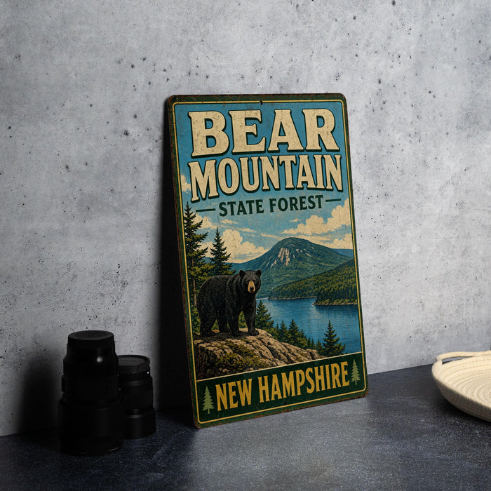 A vintage-style metal sign for Bear Mountain State Forest in New Hampshire, featuring a bear standing on a rocky outcropping overlooking a lake surrounded by pine trees.