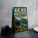 A vintage-style metal sign for Bear Mountain State Forest in New Hampshire, featuring a bear standing on a rocky outcropping overlooking a lake surrounded by pine trees.