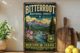 A vintage-style poster of the Bitterroot National Forest in Montana and Idaho, featuring a scenic mountain landscape with a river and pine trees.