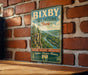 A vintage-style metal sign with the text "BIXBY STATE PRESERVE Iowa" is displayed on a brick wall.