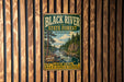 A vintage metal sign for the Black River State Forest in Wisconsin, featuring a scenic illustration of a river surrounded by pine trees and mountains.