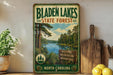 A vintage-style sign for Bladen Lakes State Forest in North Carolina, featuring a scenic image of the lake surrounded by pine trees and a blue sky.