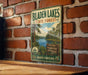 A vintage metal sign for Bladen Lakes State Forest, featuring a scenic image of the lake surrounded by pine trees and mountains.
