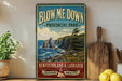 A vintage-style sign for "Blow Me Down Provincial Park" in New Brunswick, Canada, featuring a scenic coastal landscape with rocky cliffs, pine trees, and the ocean.