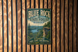 A vintage-style metal sign for the Blue Rock State Forest in Ohio, featuring a scenic image of a forest and a lake.