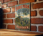 A vintage-style metal sign with the text "BOHEMIAN PARADISE PARK" and a landscape illustration of a mountainous area, mounted on a brick wall.