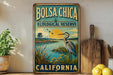 A vintage-style metal sign for the Bolsa Chica Ecological Reserve in California, featuring a bird and a sunset landscape.