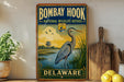 A vintage-style metal sign for the Bombay Hook National Wildlife Refuge in Delaware, featuring an illustration of a heron and a lighthouse.