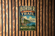 A vintage metal sign for the Border Route Trail in Minnesota, featuring a scenic image of a forest and a river.