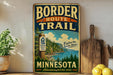 A vintage-style metal sign for the Border Route Trail in Minnesota, featuring a scenic image of a forest and a lake.