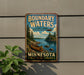 A vintage-style metal sign advertising Boundary Waters, a cultural landscape in Minnesota, featuring a canoe on a lake surrounded by pine trees.