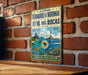a vintage-style metal sign with a brick wall backdrop, depicting a tropical beach scene with a lighthouse and palm trees.