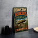 A vintage-style metal sign for the Broxton Rocks Forest in Georgia, featuring a large rock formation and surrounded by trees and flowers.