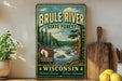 A vintage-style metal sign for the Brule River State Forest in Wisconsin, featuring a scenic illustration of the river surrounded by pine trees and mountains.
