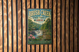 A vintage metal sign for Brush Creek State Forest in Ohio, featuring a scenic image of a waterfall surrounded by lush greenery.