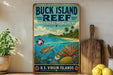 A vintage-style metal sign for Buck Island Reef National Monument, featuring a tropical beach scene with a sea turtle, coral, and other marine life.