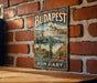 A vintage-style metal sign with the text "Budapest" and "Budapest, Hungary" displayed on it, hanging on a brick wall.