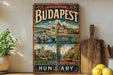 A vintage-style poster of Budapest, Hungary, featuring various landmarks and scenes, is displayed on a wall next to a wooden cutting board and some potted plants.