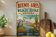 A vintage-style sign for the Buenos Aires National Wildlife Refuge in Arizona, featuring an illustration of a heron, cactus, and flowers against a desert landscape.