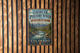 A vintage metal sign for the Cache La Poudre River National Heritage Area in Colorado, featuring a scenic illustration of the river surrounded by mountains and forests.