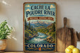 A vintage-style sign for the Cache la Poudre River National Heritage Area in Colorado, featuring a scenic mountain landscape with a flowing river.