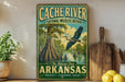 a vintage-style sign for the Cache River National Wildlife Refuge in Arkansas, with a painting of a bird flying over a swampy landscape.