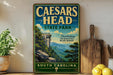 a vintage-style sign for Caesars Head State Park in South Carolina, with a scenic mountain landscape and a wooden cutting board on a shelf.