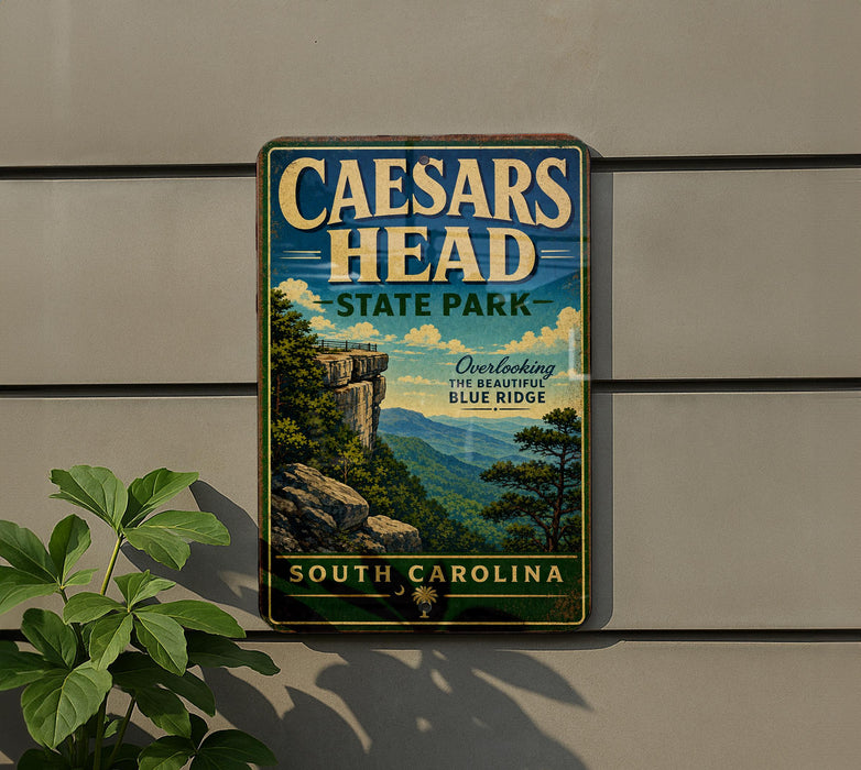 a vintage-style metal sign for Caesars Head State Park in South Carolina, with a scenic mountain landscape and a cliff on the left side.