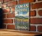 A vintage-style sign for Camas Prairie, a cultural landscape in Idaho, is displayed on a brick wall.