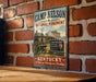 A vintage-style metal sign for the Camp Nelson National Monument in Kentucky, featuring an illustration of a log cabin and a cannon, mounted on a brick wall.