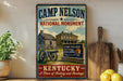 A vintage-style sign for the Camp Nelson National Monument in Kentucky, featuring a cabin and cannon, with a wooden paddle and lemons on a shelf in the foreground.