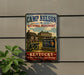 A vintage-style metal sign for the Camp Nelson National Monument in Kentucky, featuring a cannon and a wooden cabin, mounted on a gray wall.