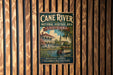 A vintage-style metal sign for the Cane River National Heritage Area in Louisiana, featuring a building and palm trees, is displayed on a wooden wall.