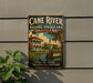 A vintage-style sign for the Cane River National Heritage Area in Louisiana, featuring a building and a boat on the water.
